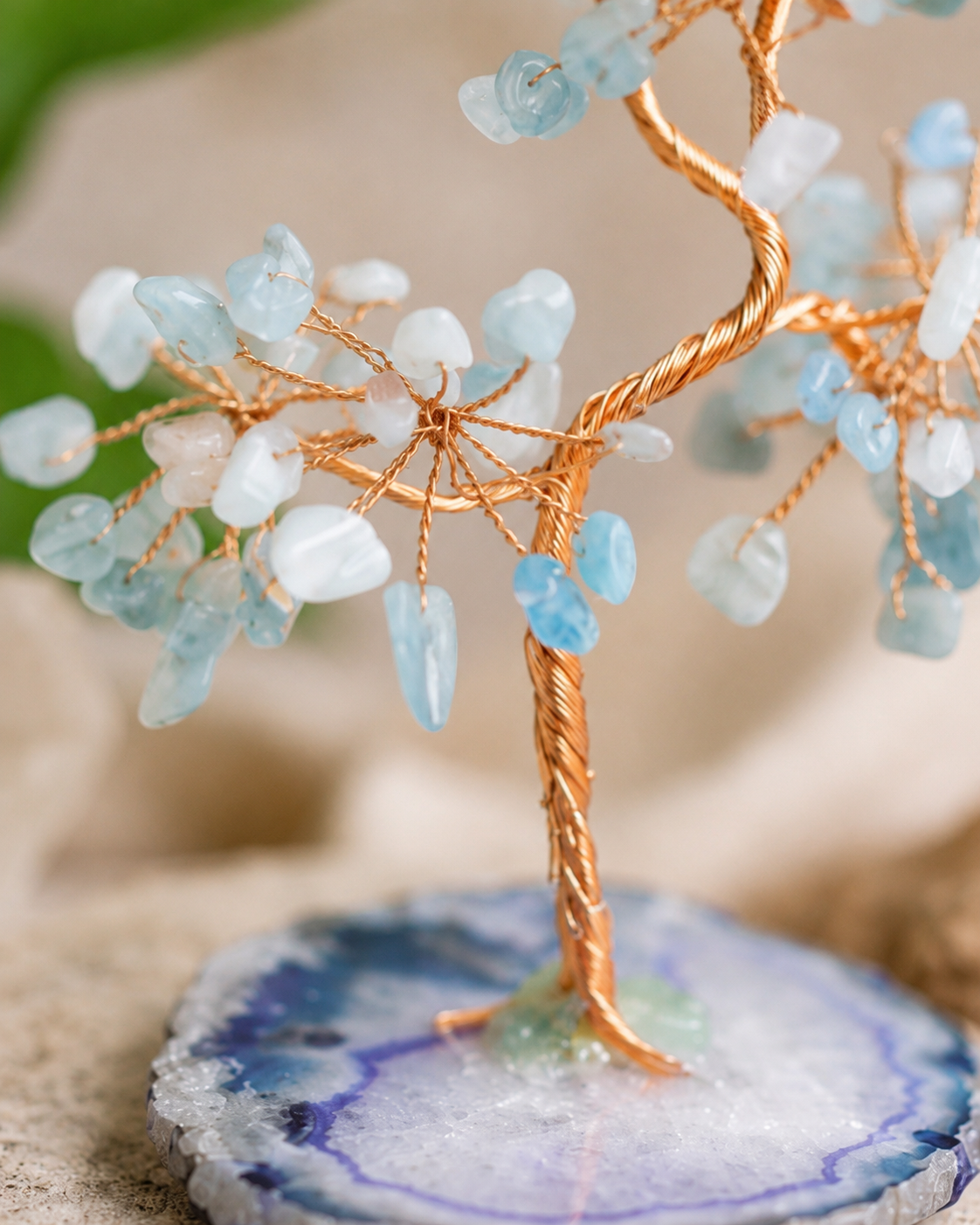 Decorative tree sculpture with blue and white stones on a natural stone base