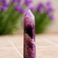 Amethyst crystal tower on a stone surface with blurred purple flowers in the background