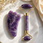 Purple jade roller and gua sha tool on a marble surface with dried flowers.
