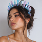 Woman wearing a colorful crystal crown against a plain background