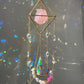 Decorative hanging crystal with pink stone and colorful beads against a reflective background