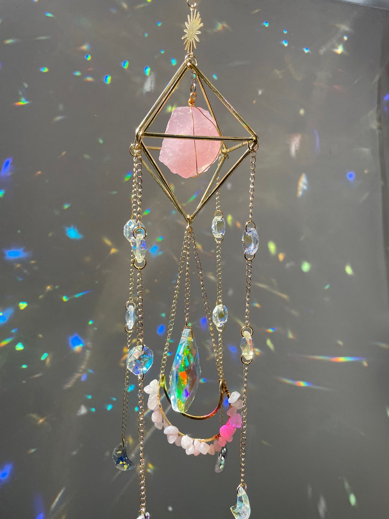 Decorative hanging crystal with pink stone and colorful beads against a reflective background