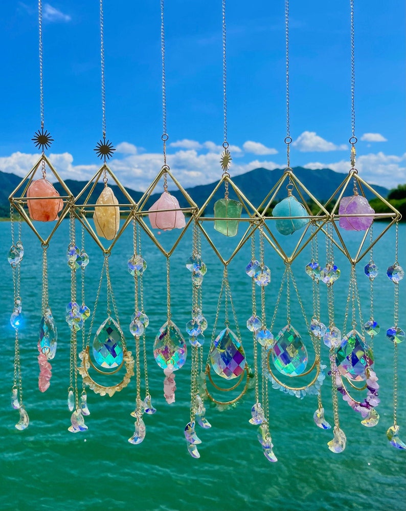 Decorative hanging crystal mobile with colorful stones against a blue sky and water background