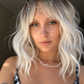 A close-up portrait of a woman with platinum blonde wavy hair wearing a silver crescent moon and star headpiece with blue and white crystal-like accents, along with a beaded necklace and a black-and-white patterned top.