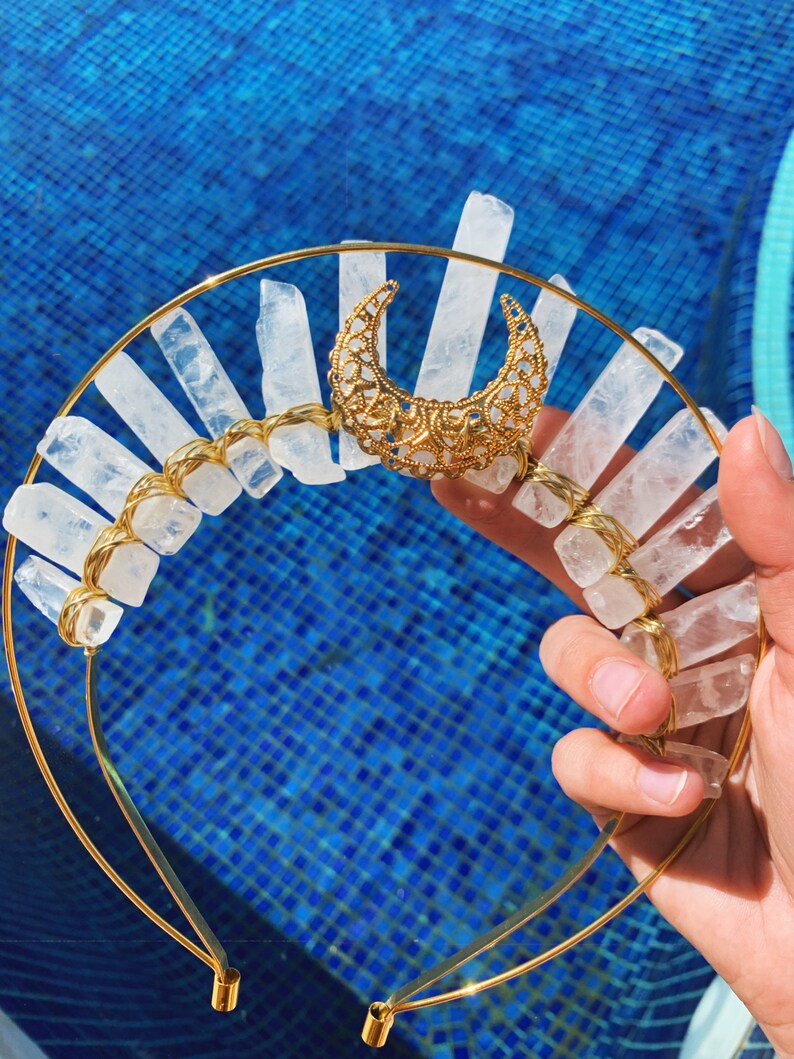 Gold headband with crystal accents held by a hand against a blue tiled background