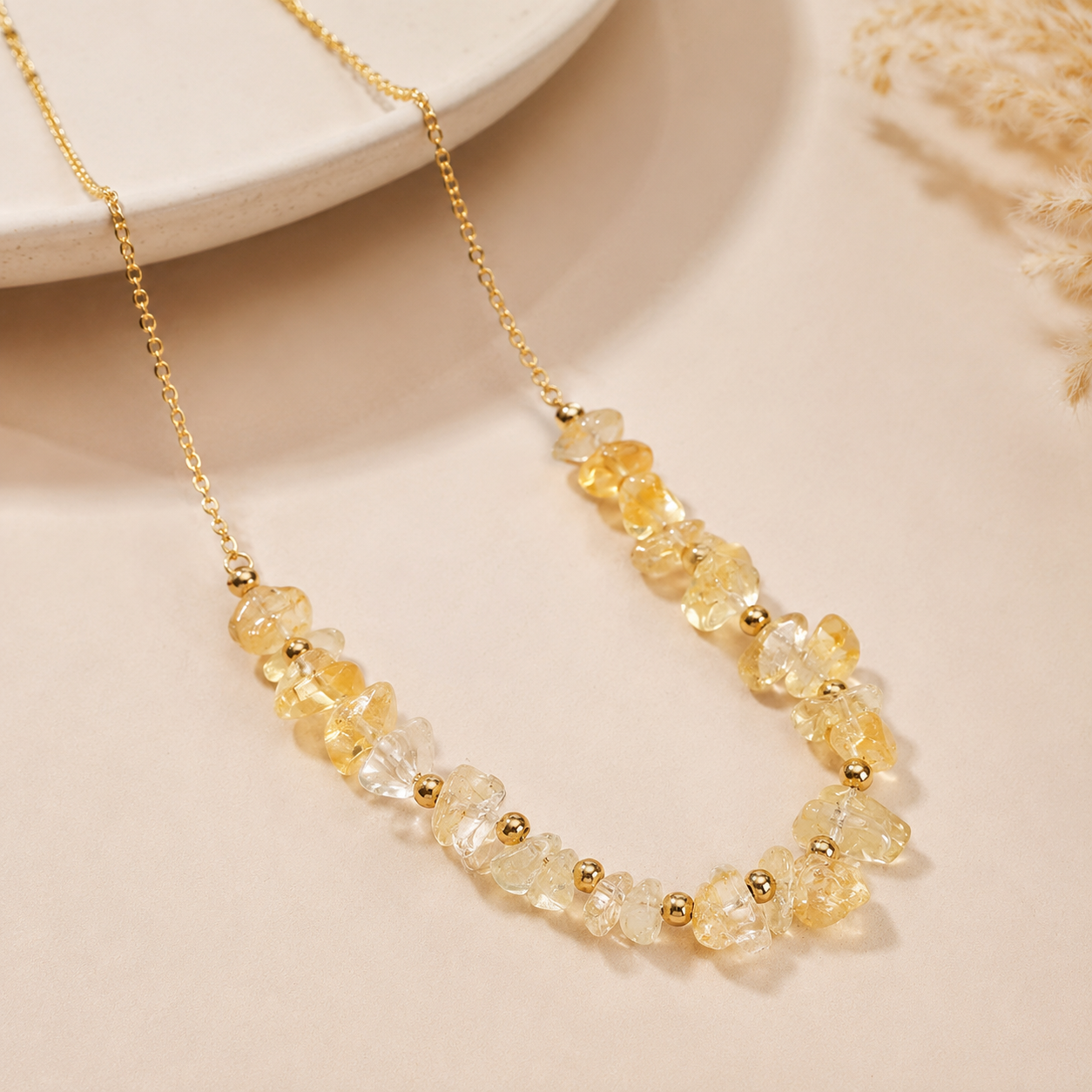 A gold chain necklace featuring a strand of clear, faceted crystal beads and small gold spacer beads, displayed on a warm beige surface.