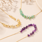 Three delicate gold chain necklaces with chunky gemstone beads in yellow, light green, and purple, arranged on a light beige background with soft shadows.