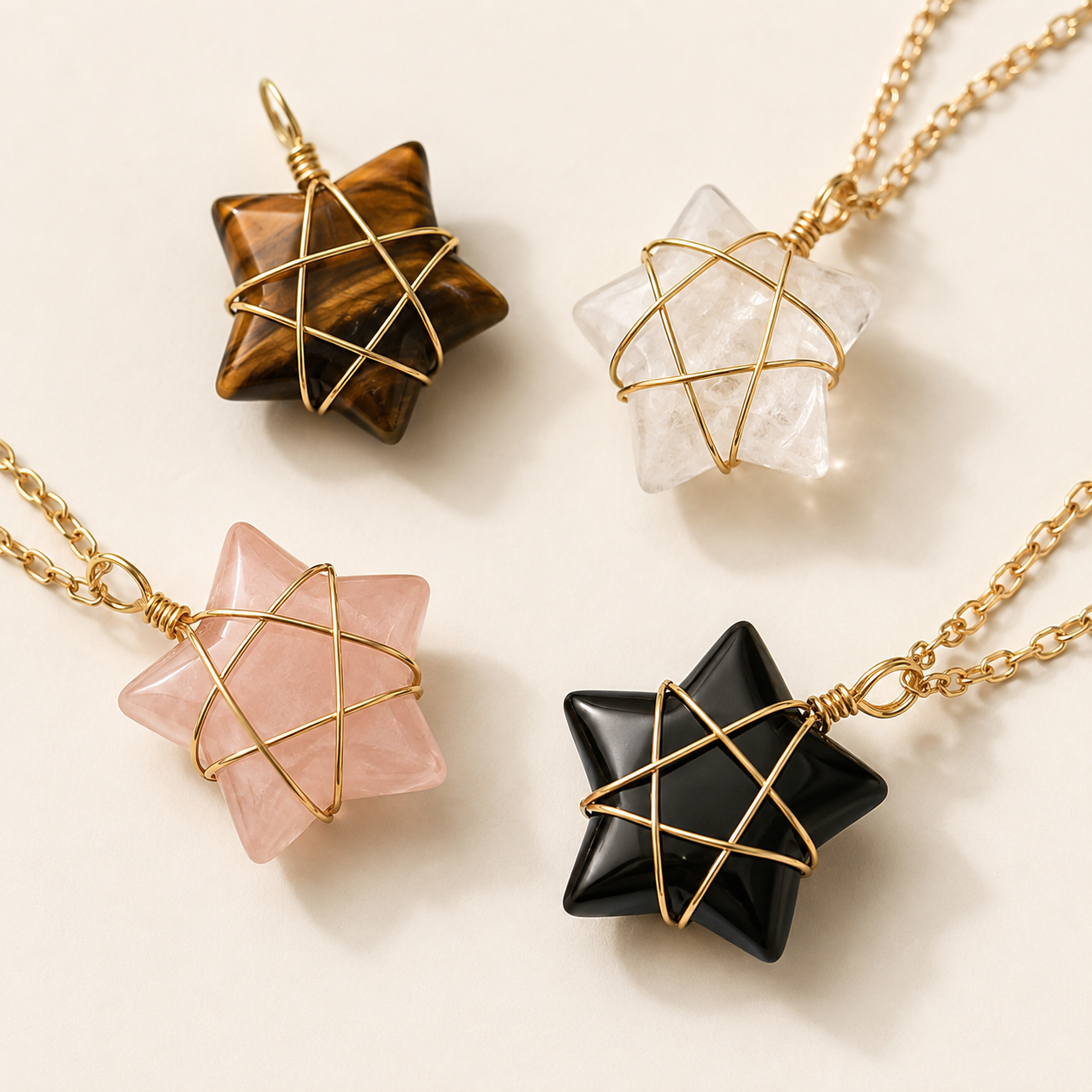 Four star-shaped crystal pendants with gold wire mesh and gold chains, arranged on a light cream background. The crystals are brown tiger's eye, clear quartz, pink rose quartz, and black obsidian.