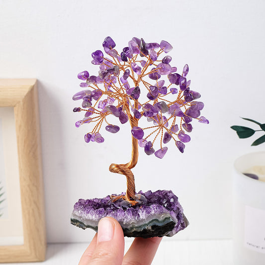 Amethyst crystal tree on a purple crystal base held by a hand against a light background