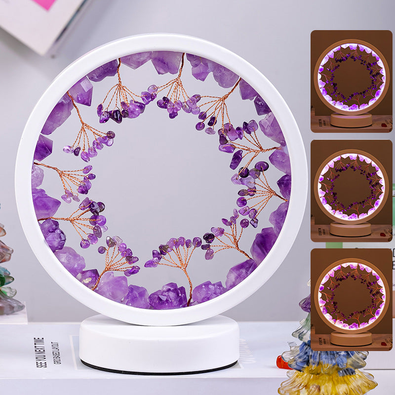 Round decorative item with purple stones and branches on a white base, surrounded by additional items.