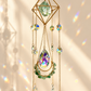 A gold geometric crystal wind chime with hanging teardrop and round beads, featuring a large iridescent teardrop and green faceted crystals, set against a warm beige wall with sunlight and rainbow reflections.