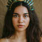 Woman wearing a decorative headpiece with green stones and gold accents against a neutral background