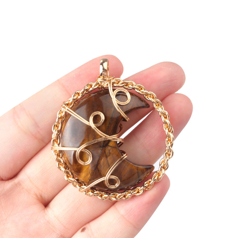 Hand holding a gold-framed pendant with a brown stone on a white background