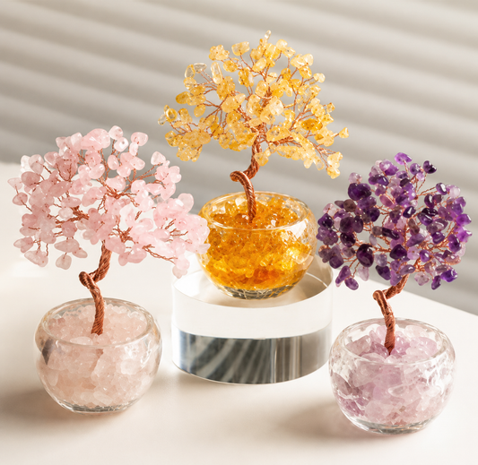Three crystal bonsai trees in glass containers on a white surface with a neutral background