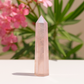 Rose quartz crystal on a white surface with pink flowers and green leaves in the background
