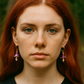 Woman with red hair wearing earrings against a blurred natural background