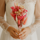 Person wearing a white lace dress holding a bouquet of pink flowers.