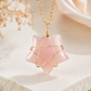 A pink rose quartz star pendant necklace with a gold wire star design wrapped around the center, hanging from a gold link chain on a soft, light beige background.