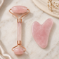 Pink jade roller and gua sha tool on a marble surface with a decorative plate and flowers.