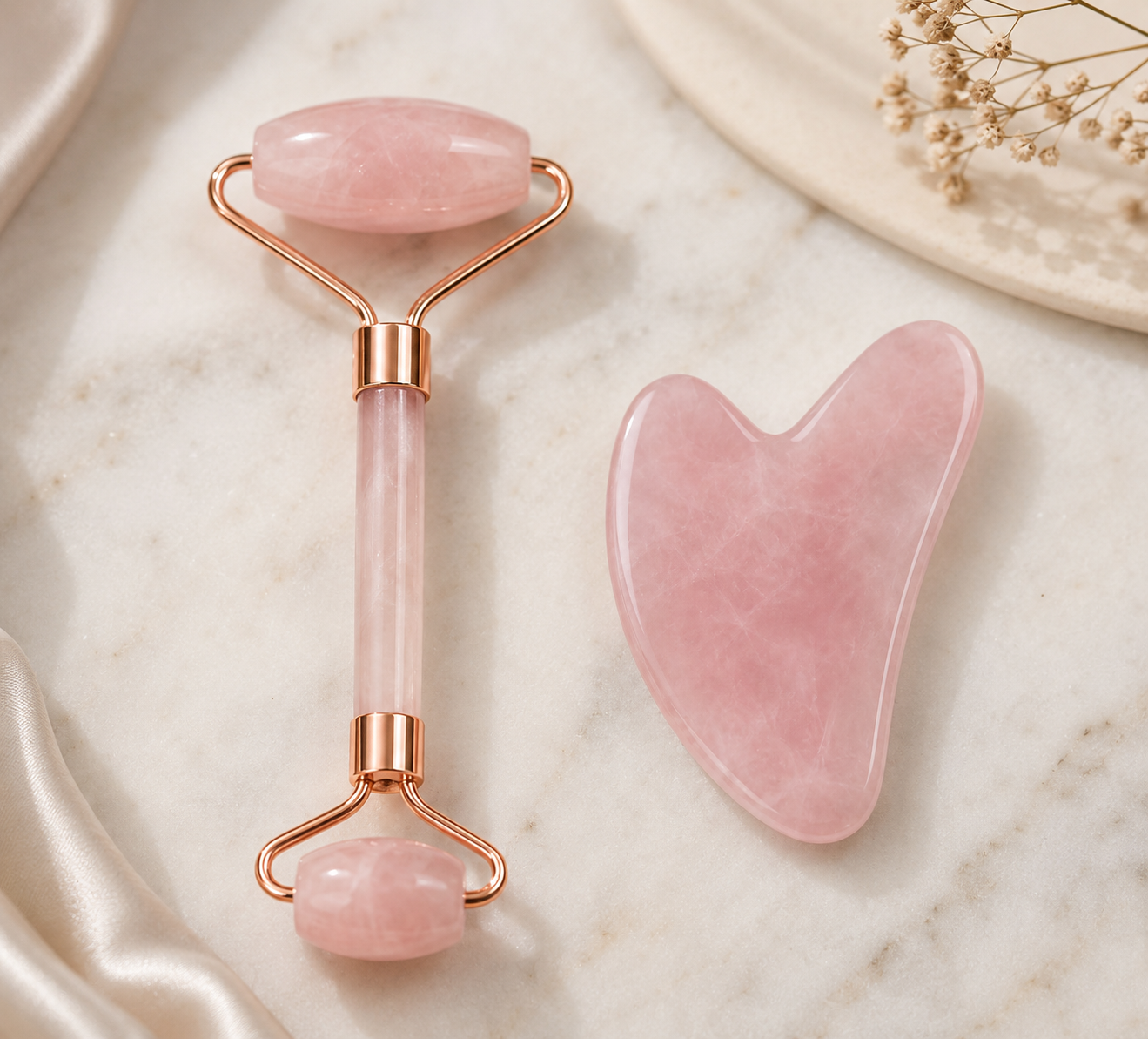 Pink jade roller and gua sha tool on a marble surface with a decorative plate and flowers.