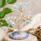 Decorative crystal tree on a natural stone base with green leaves and rocks in the background