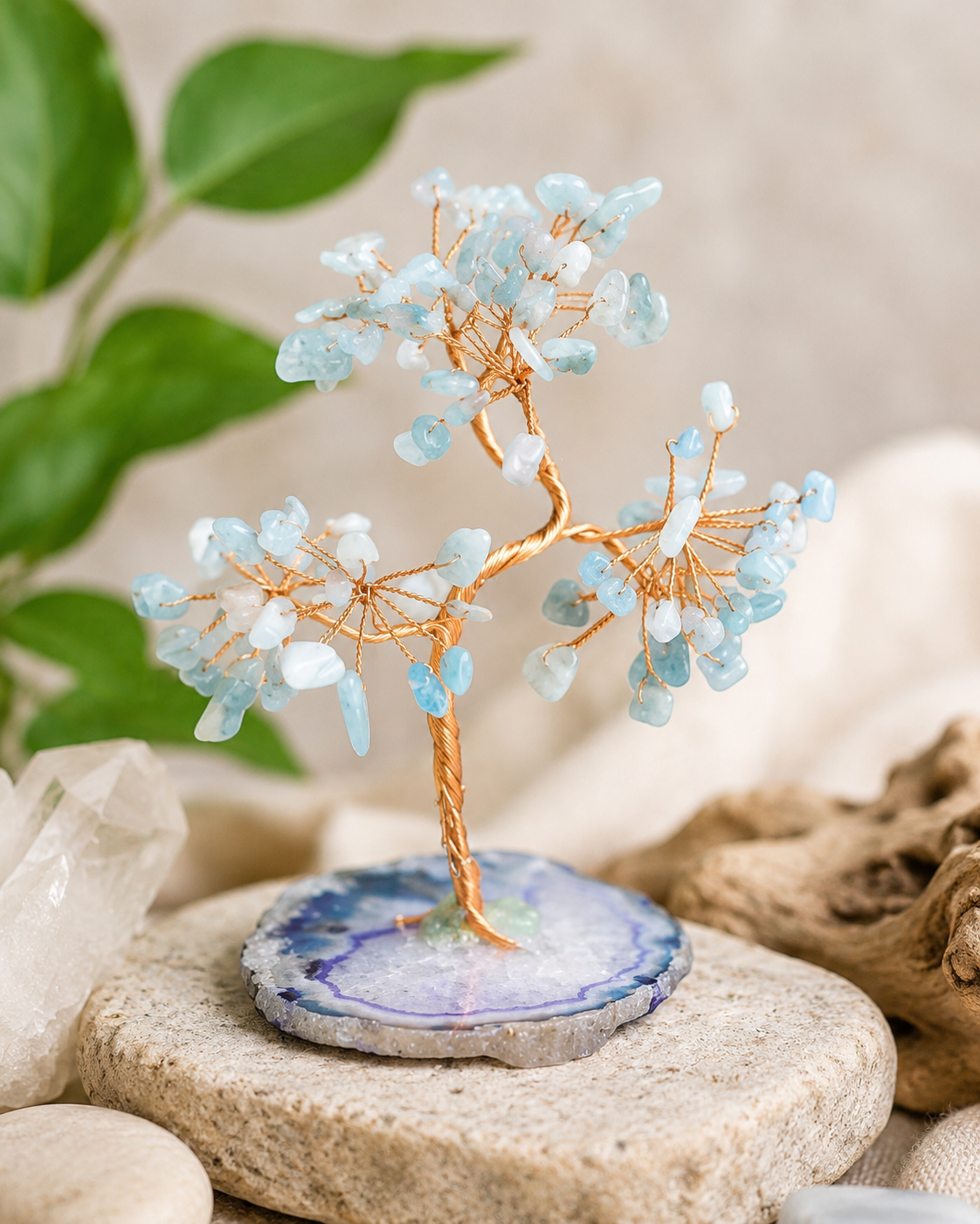 Decorative crystal tree on a natural stone base with green leaves and rocks in the background