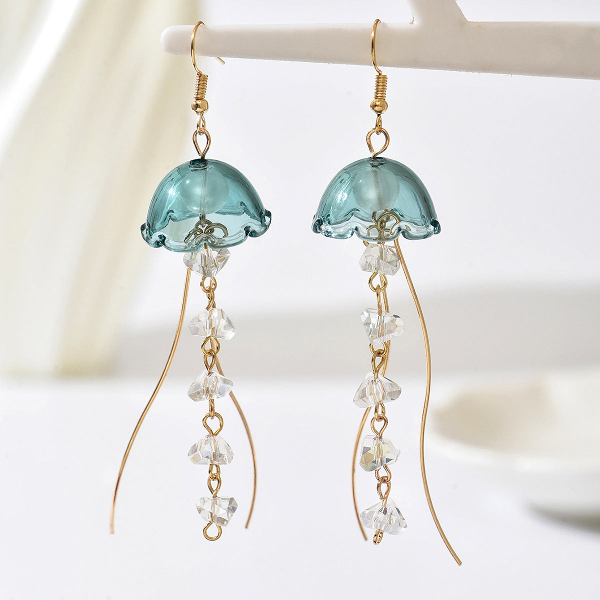 Jellyfish-shaped earrings with blue tops and crystal-like beads on a white background
