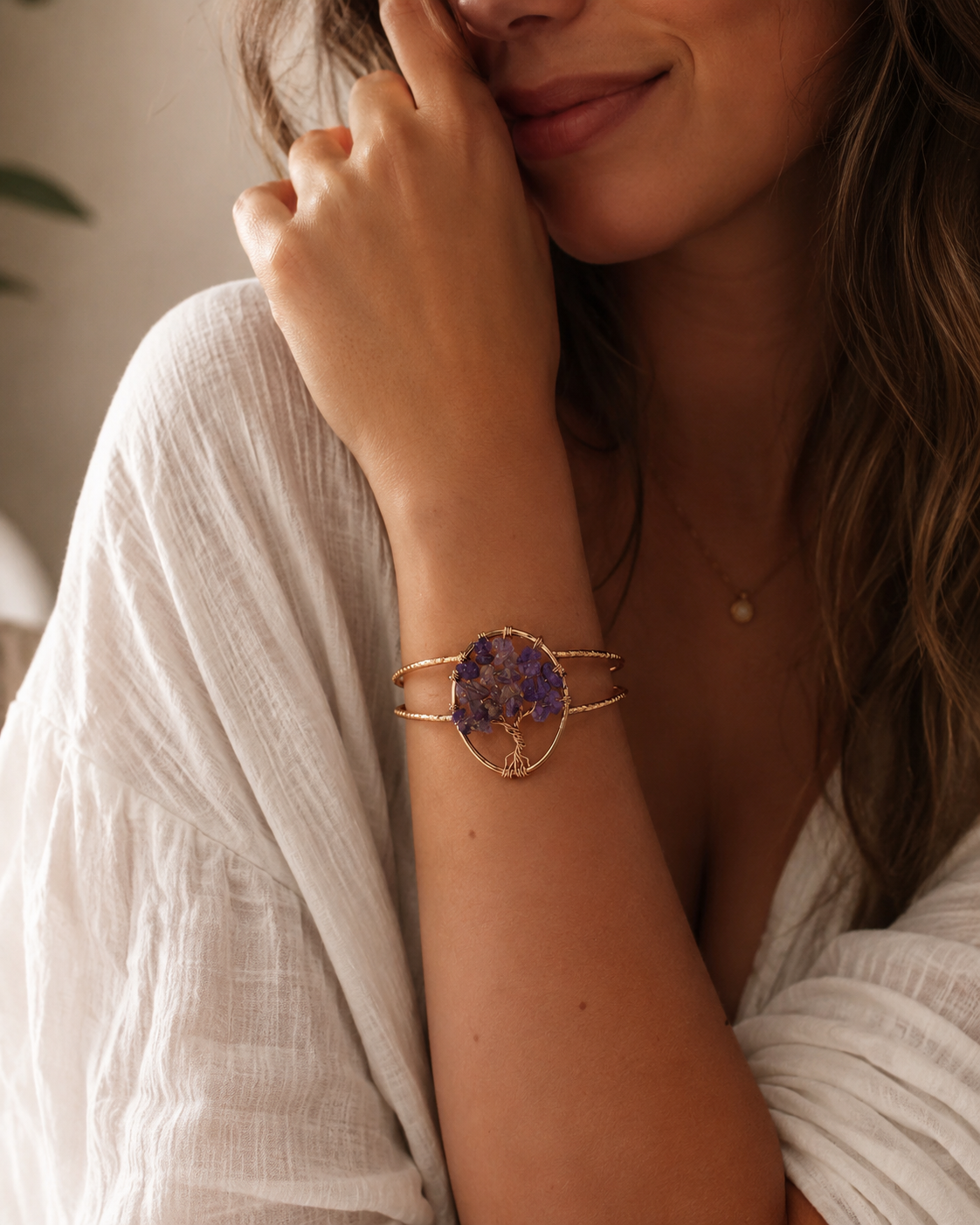 A close-up lifestyle shot of a woman wearing a gold-toned double-band cuff bracelet with a central purple amethyst crystal tree motif.